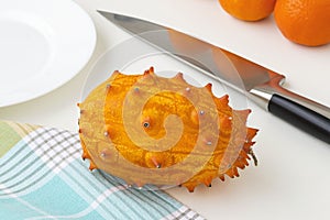 Fresh orange kiwano cucumis metuliferus, horned melon and sharp chef knife on a kitchen table. Fruits, vegetables, vegetarian