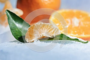 Fresh orange mandarin fruit with green leaves are frozen on cold blue ice.