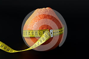 Fresh orange wrapped with measuring tape on a black background. The waist circumference of an orange is 120 cm. The