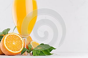 Fresh oranges juice in wineglass with ripe half oranges and green leaf on soft white wood table, copy space, closeup.