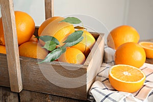 Fresh oranges with leaves and rustic box on table