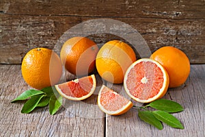 Fresh oranges with slices and leaves on wooden background. photo