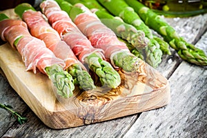 Fresh organic asparagus wrapped in Parma ham on a cutting board