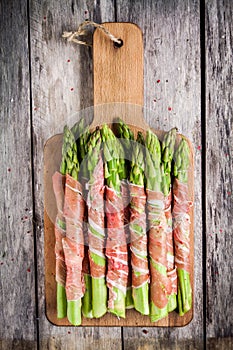 Fresh organic asparagus wrapped in prosciutto on a cutting board