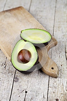 Fresh organic avocado halves on cutting board on old wooden table background