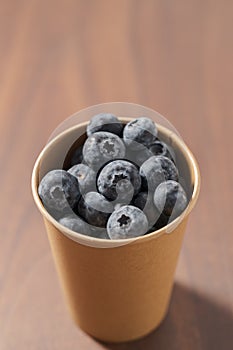 Fresh organic blueberries in papaer cup on wood table with copy space