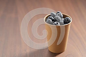 Fresh organic blueberries in papaer cup on wood table with copy space