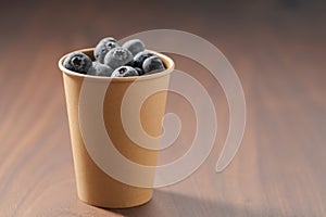 Fresh organic blueberries in papaer cup on wood table with copy space