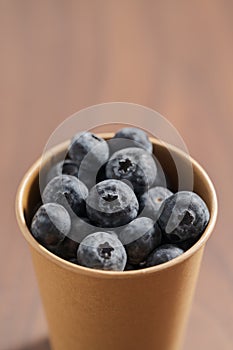 Fresh organic blueberries in papaer cup on wood table with copy space