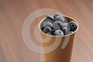 Fresh organic blueberries in papaer cup on wood table with copy space