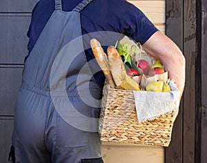 Fresh organic food in a wicker basket in the hands of a bicycle courier. Bike delivery or donation of food concept