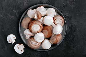 Fresh organic brown and white champignon mushrooms in bowl on dark stone background