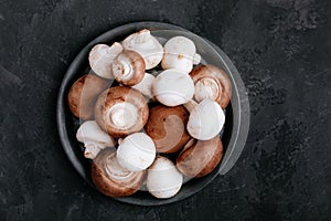 Fresh organic brown and white champignon mushrooms in bowl on dark stone background