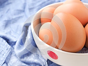 Fresh organic eggs in bowl on blue fabric background.