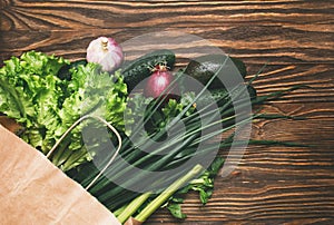 Fresh organic food in crafting paper bag, fresh vegetables. Salad, cucumber, celery, onion, avocado and parsley on wooden