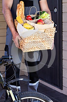 Fresh organic food in a wicker basket in the hands of a bicycle courier. Bike delivery or donation of food concept