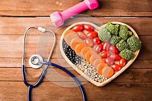 Fresh organic fruits and vegetables in heart plate wood, dumbbell and doctor stethoscope