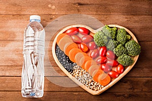 Fresh organic fruits and vegetables in heart plate wood and plastic water bottles
