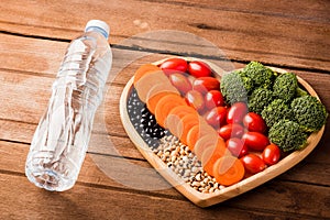 Fresh organic fruits and vegetables in heart plate wood and plastic water bottles