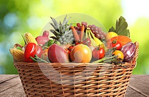 Fresh organic fruits and vegetables in wicker basket on wooden table, closeup