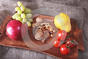 Fresh organic fruits and vegetables on wooden Serving tray. Assorted apple, pear, grapes, tomatoes and nuts.