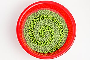 Fresh organic green peas in a large red round bowl isolated on white, top view