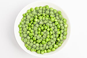 Fresh organic green peas in a white round bowl on a table in soft focus, isolated on white, top view