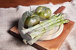 Fresh and organic green tomatoes and some asparagus, on a wooden table