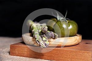 Fresh and organic green tomatoes and some asparagus, on a wooden table