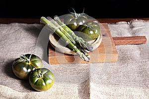 Fresh and organic green tomatoes and some asparagus, on a wooden table