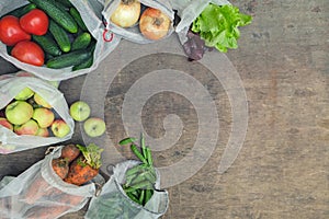 Fresh organic groceries in reusable recycled mesh produce bags on wooden background with copy space. Zero waste shopping concept.