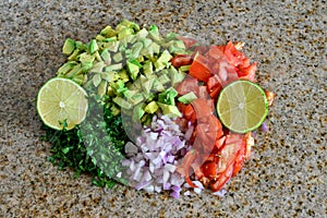 Fresh organic ingredients chopped for salsa, avocado, tomato, lime. on granite kitchen counter.