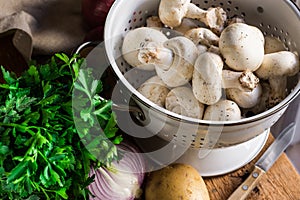 Fresh organic ingredients for preparing healthy vegetarian meal potatoes, mushrooms in colander, halved onion, parsley