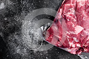 Fresh organic meat of lamb or mutton vacuum packed, on black dark stone table background, top view flat lay, with copy space for