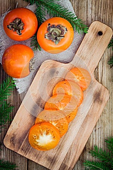 Fresh organic persimmon with slices on wooden board