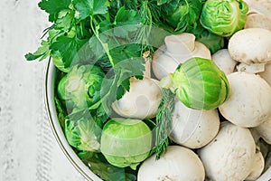 Fresh Organic Produce Vegetables Brussels Sprouts Green Herbs Parsley Dill Mushrooms in White Metal Colander on Wooden Garden Tabl
