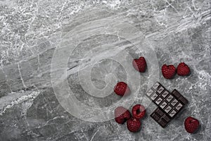 Fresh organic raspberries and two bars of organic 70% cocoa dark chocolate on a marble background with copy space