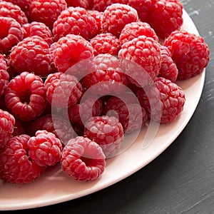 Fresh organic raspberry on a pink plate on black surface, low angle view. Close-up. Copy space