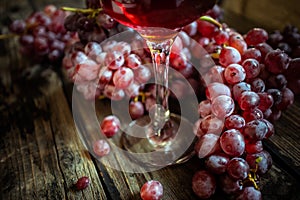 Fresh organic red grape and glass of wine on old wooden table