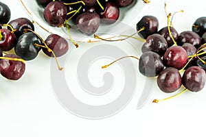 Fresh organic ripe black cherries in a bowl and spread around on an isolated white background