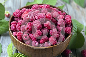 Fresh organic ripe raspberry with leaf in bowl on wooden table photo