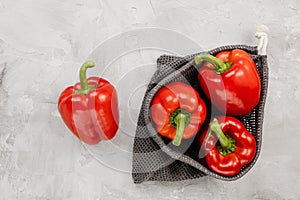 Fresh organic ripe sweet red bell pepper in eco-friendly reusable produce bag on gray, copy space