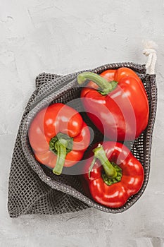 Fresh organic ripe sweet red bell pepper in eco-friendly reusable produce bag on gray, copy space