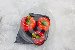 Fresh organic ripe sweet red bell pepper in eco-friendly reusable produce bag on gray, copy space