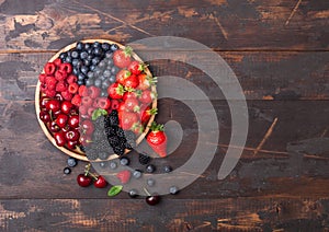 Fresh organic summer berries mix in round wooden tray on dark wooden table background. Raspberries, strawberries, blueberries,