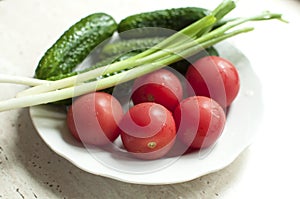Fresh organic tomatoes and cucumbers with green onions on a white plate