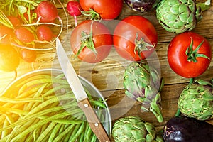 Fresh organic vegetables artichokes green beans tomatoes red radish eggplants on wood garden kitchen table. Summer autumn harvest