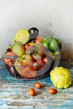 Fresh organic vegetables in a basket on a gray background. Harvest of pepper, tomatoes, eggplant and mini pumpkin patissons.