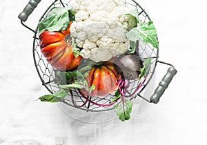 Fresh organic vegetables - cauliflower, heirloom tomatoes, beets in vintage metal basket on light background