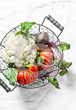 Fresh organic vegetables - cauliflower, heirloom tomatoes, beets in vintage metal basket on light background